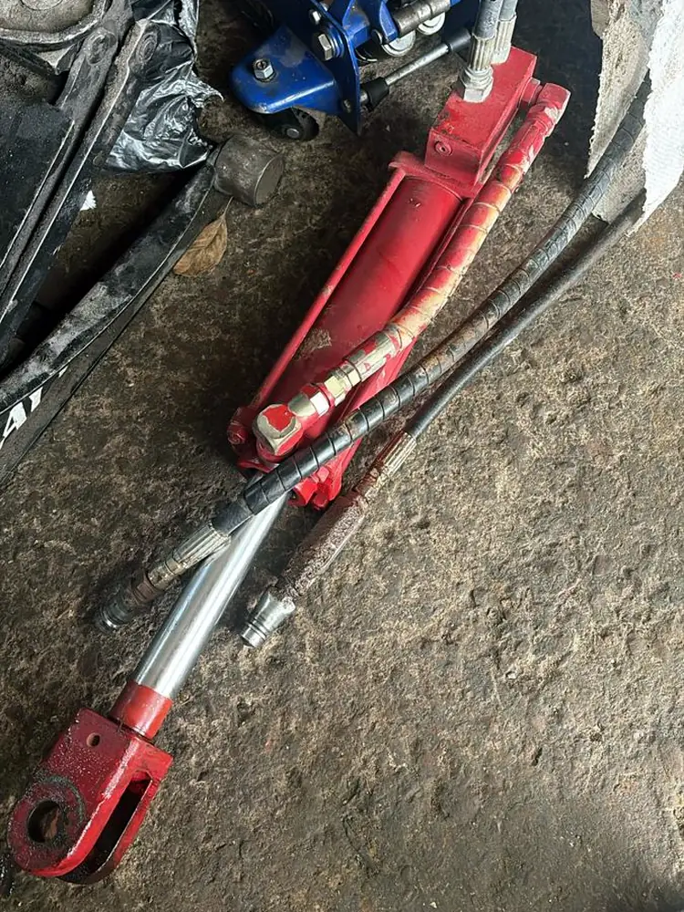 Cilindro hidráulico rojo con mangueras, tal como llegó al taller